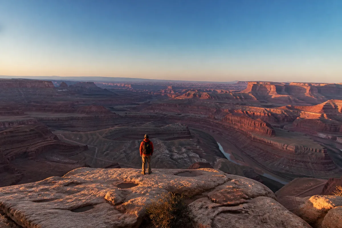 Randonneuse de dos observant un vaste canyon depuis un promontoire rocheux, ciel dégagé en fin de journée